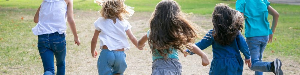 Group of kids running on grass together, having race in park. Back view, full length. Children outdoor activity concept